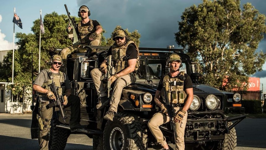 Four men wear army gear.