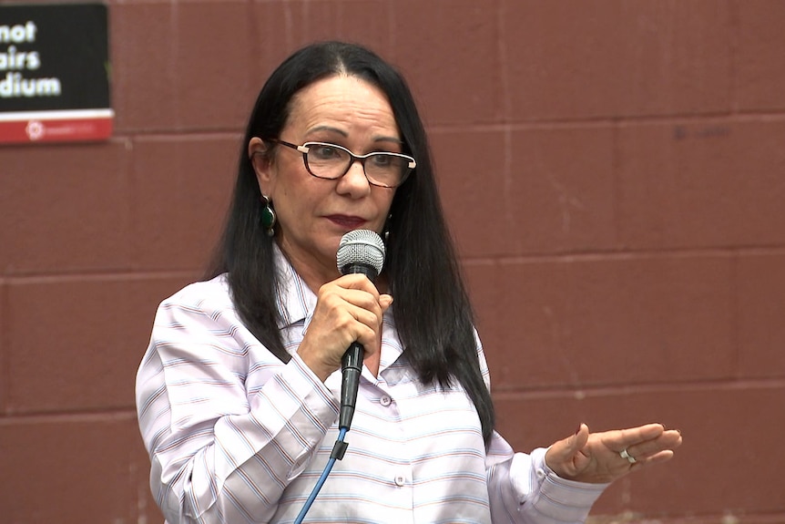 a woman wearing glasses holding a microphone about to speak