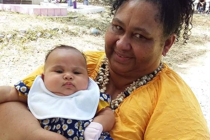 Torres Strait Islander woman sitting holding young baby.