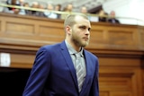 A man with a shaved head and beard wearing a suit arrives in court
