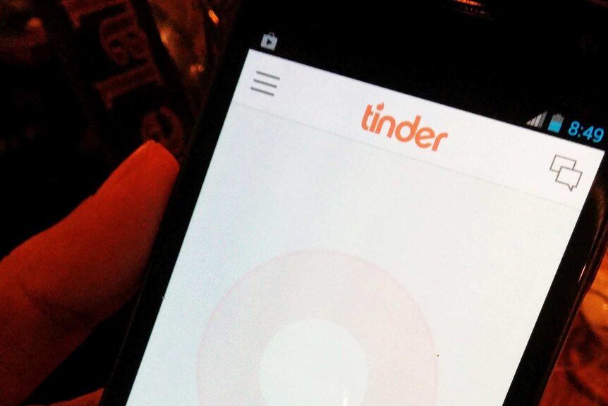 A man holds a smartphone displaying the application Tinder