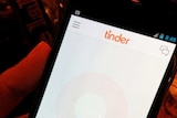 A man holds a smartphone displaying the application Tinder