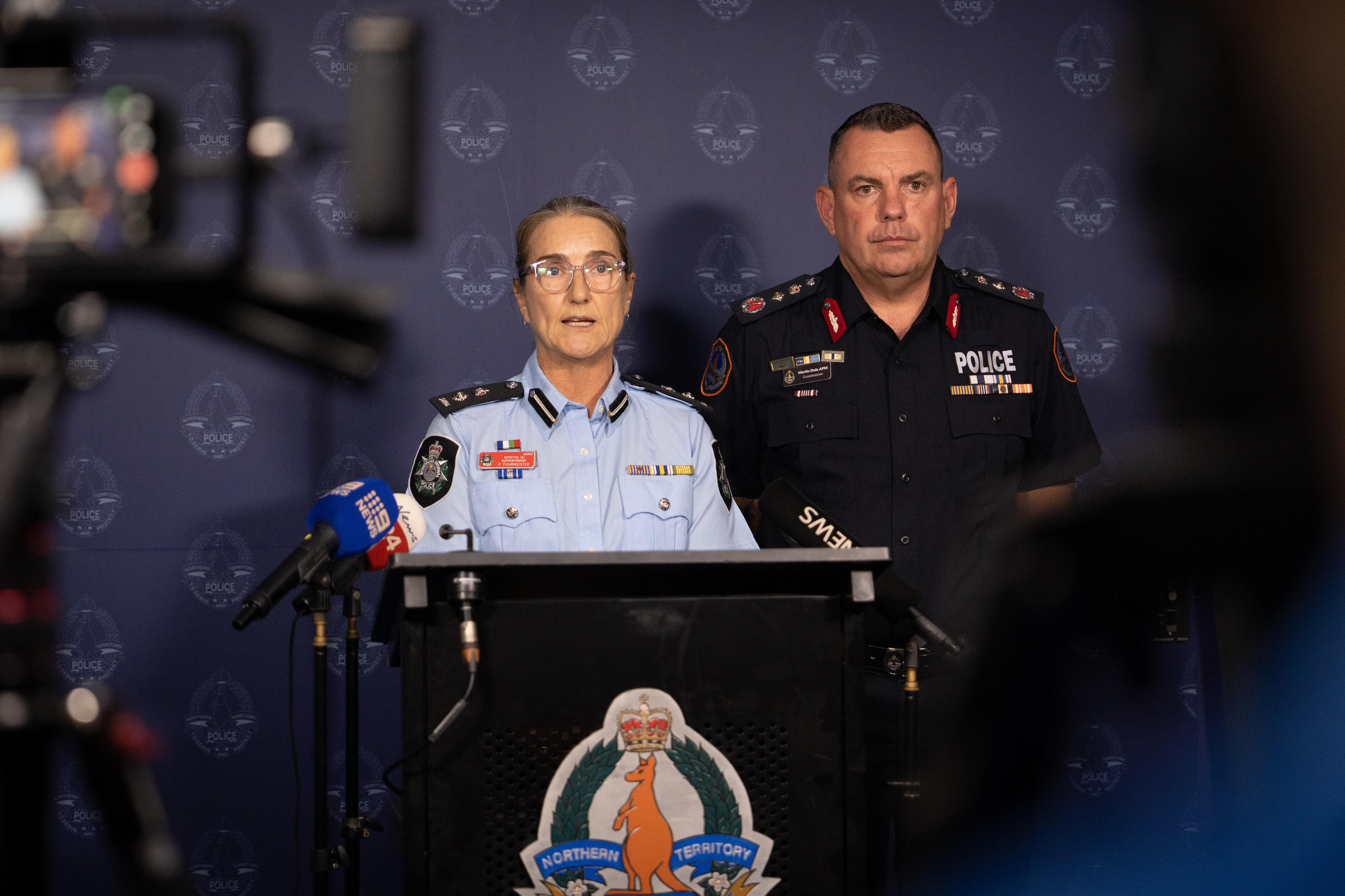 A man and woman in police uniforms speaking from a lectern to the media, at a press conference.