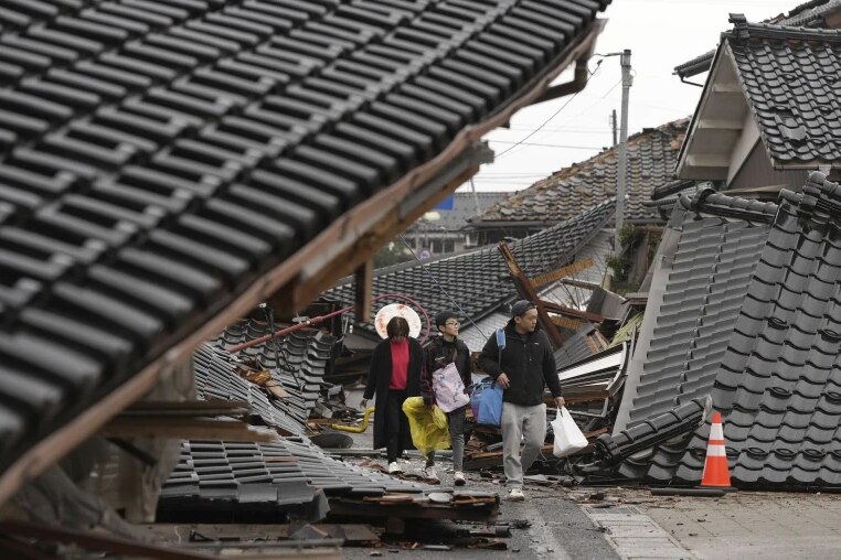 Three people walk through destroyed homes 