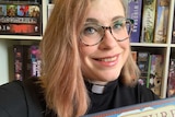 Uniting Church minister The Reverend Amanda Hay wearing a clerical collar holding her favourite board game, Viticulture.