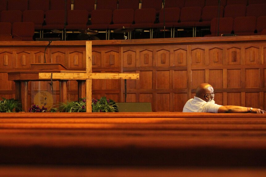 A man sitting in a church pew near a wooden cross