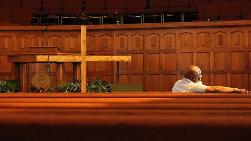 A man sitting in a church pew near a wooden cross