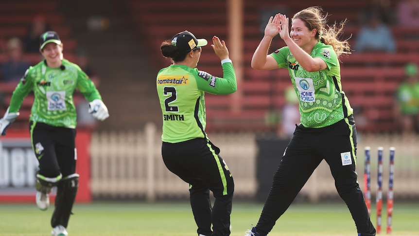 A WBBL bowler smiles and high-fives a teammate after a wicket.
