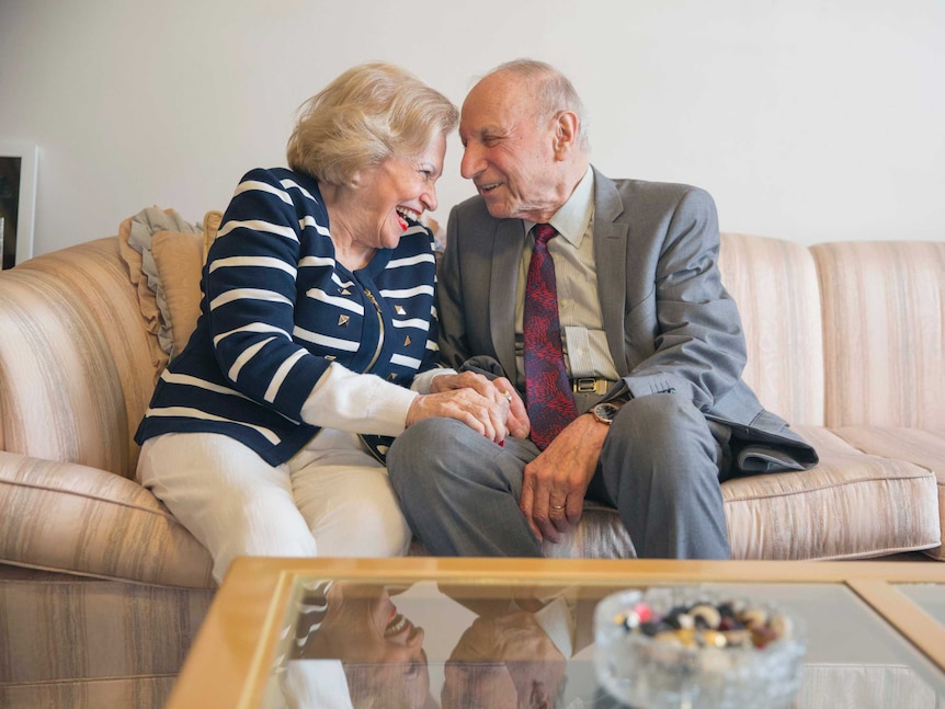 Sigi and Hanka Siegreich sit on a couch, smiling at each other.