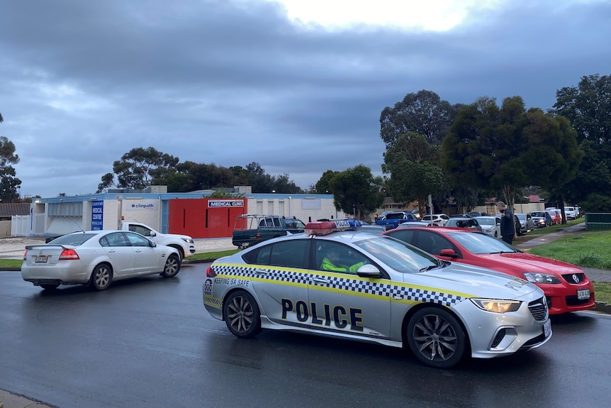 A police car in front of other cars lined up near a medical clinic