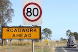 Cars drive past a roadworks sign.