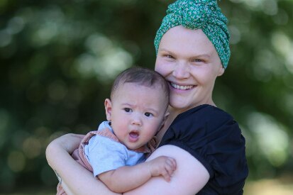 woman in scarf smiles into the camera with her baby son in her arms
