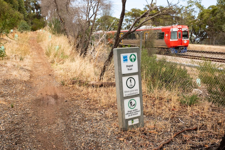 A train runs alongside a bike path on an overcast day