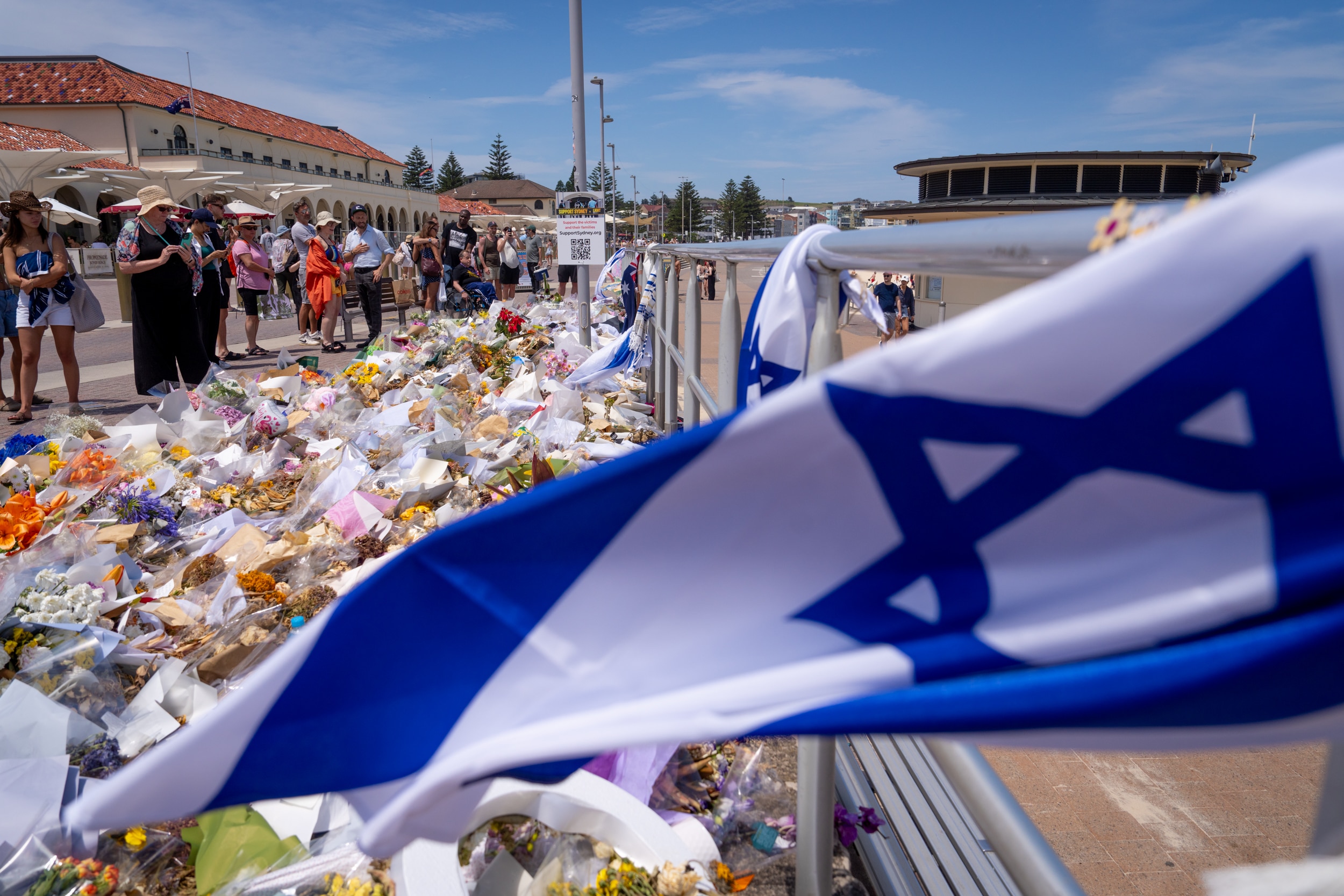 Uma bandeira israelense em frente a um grande memorial improvisado com flores próximo a uma praia.