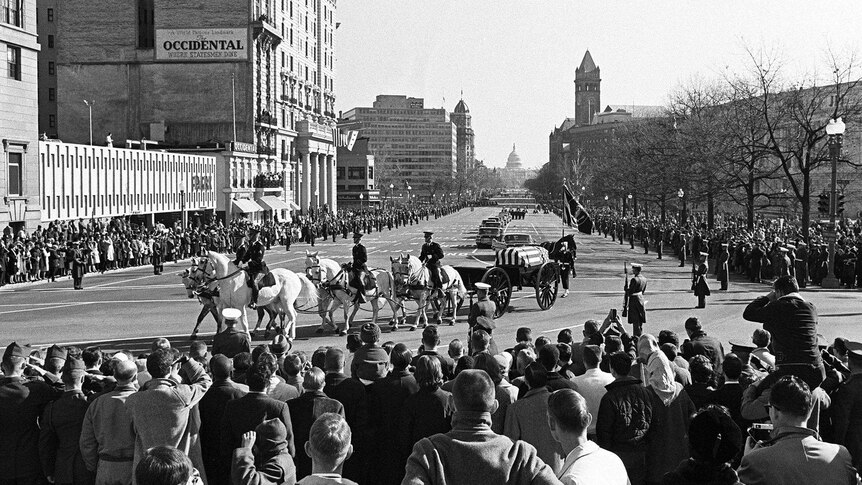 The flag-draped coffin of JFK moves through downtown Washington, DC, during his state funeral.