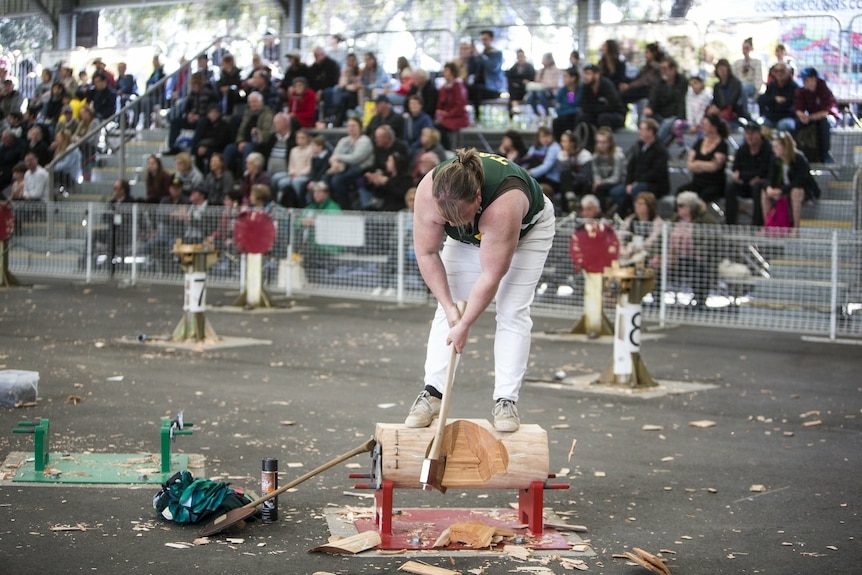 A woman competing in a woodchopping event before a crowd.