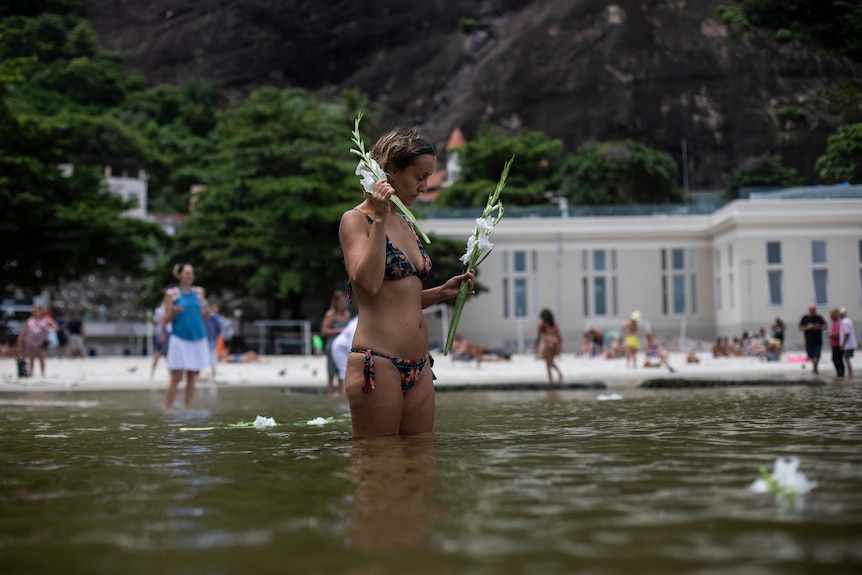 A woman in a bikini places flower offerings in the waters of Urca beach.