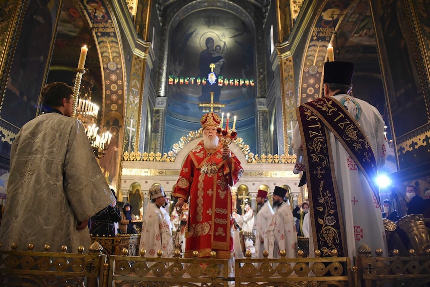 A man in a red robe walks through the aisle of a church in Ukraine.