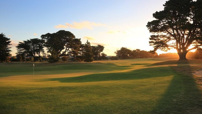 Picture of a golf course in the late afternoon sun with the flag on a green just out of the shadows.