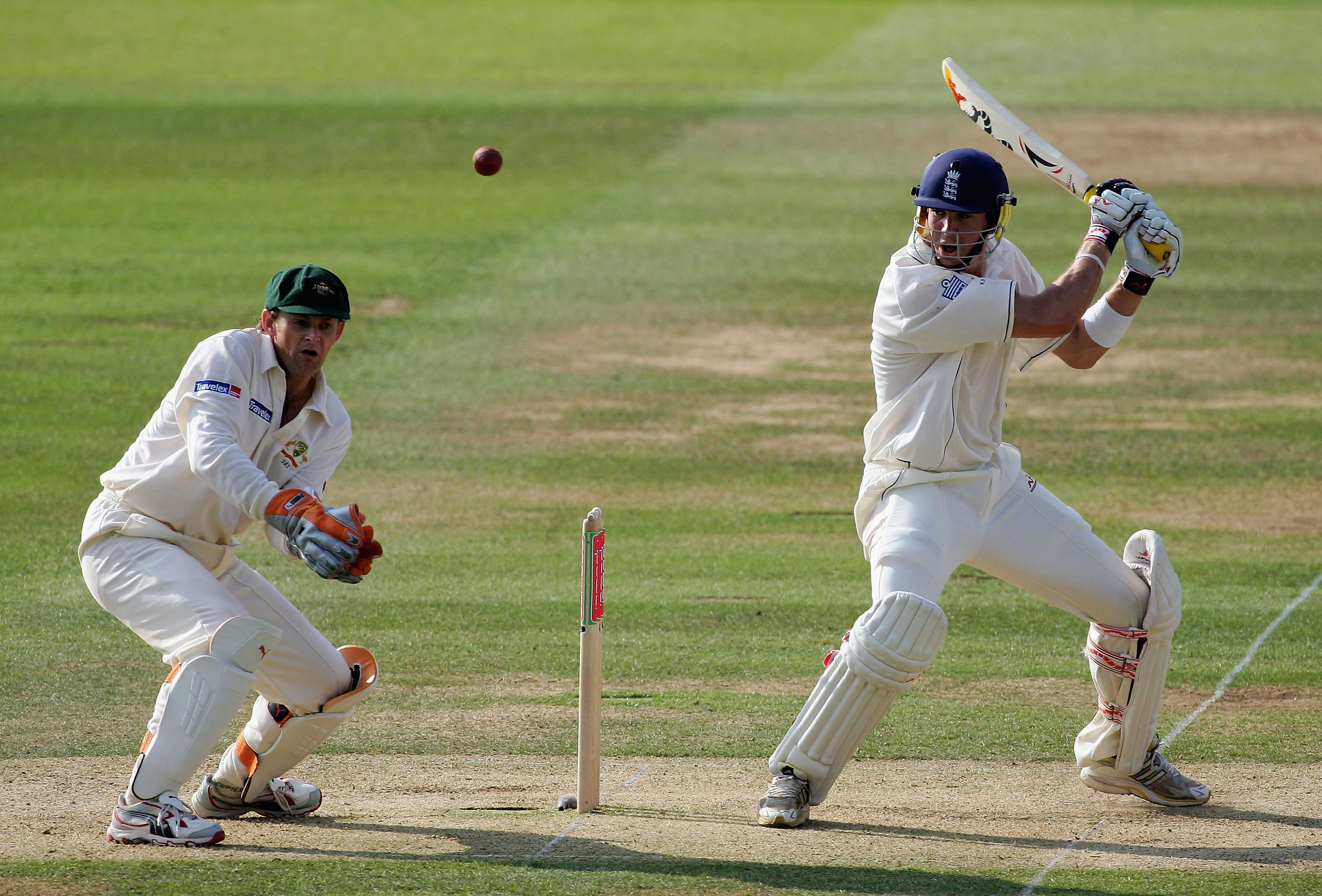 An English batsman plays a full-blooded cut shot as an Australian wicketkeeper watches from behind the stumps. 