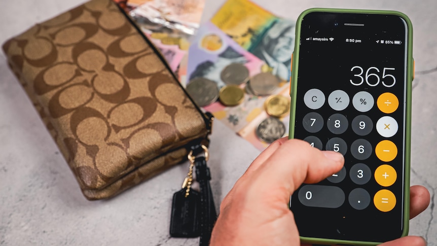 A man types numbers 365 into a phone calculator with cash and a wallet in the background