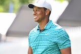 Tiger Woods smiles while walking and carrying a golf club