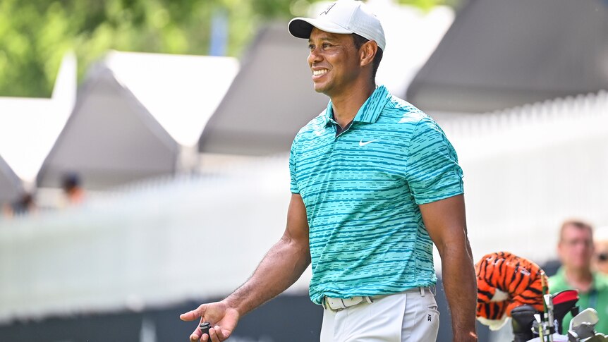 Tiger Woods smiles while walking and carrying a golf club