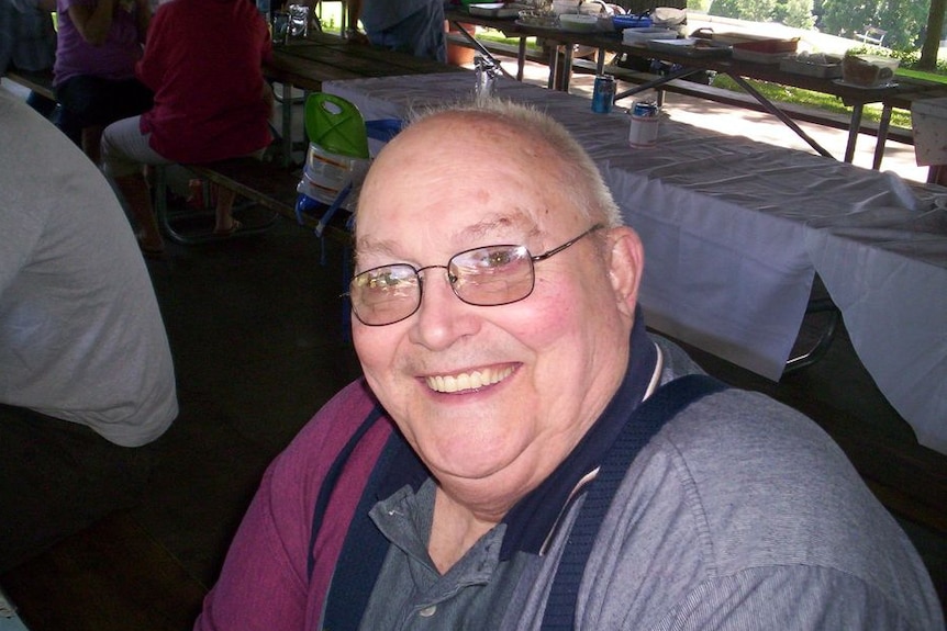 Close-up of bald man with glasses smiling, table behind him