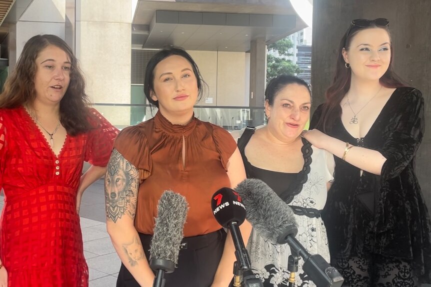 Four women stood together in front of a bank of microphones.