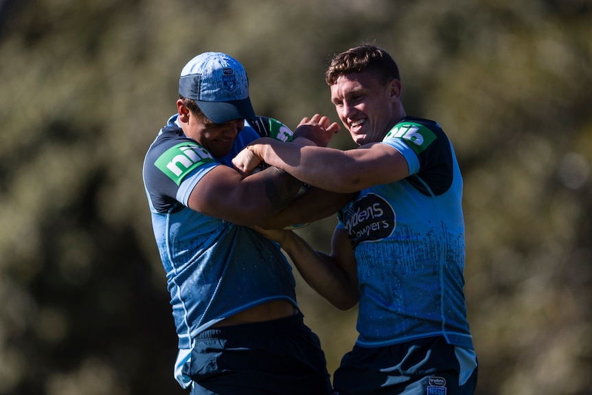 Two NSW State of Origin players smile as they wrestle together during a training session.