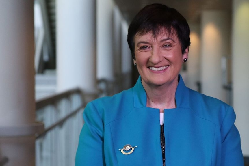 A woman with short brown hair and wearing a teal jacket smiles.