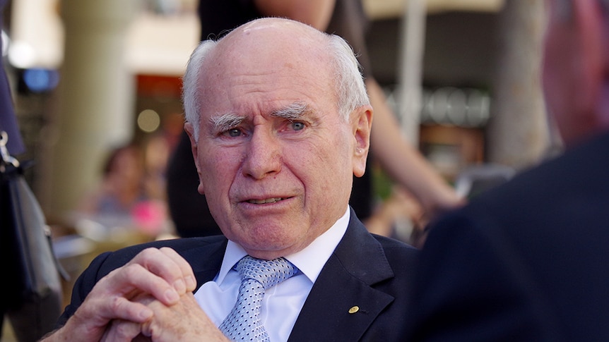 John Howard, sitting with hands clasped, looking relxed.