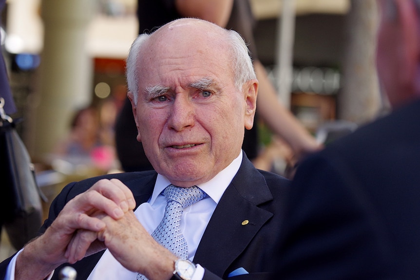 John Howard, sitting with hands clasped, looking relxed.