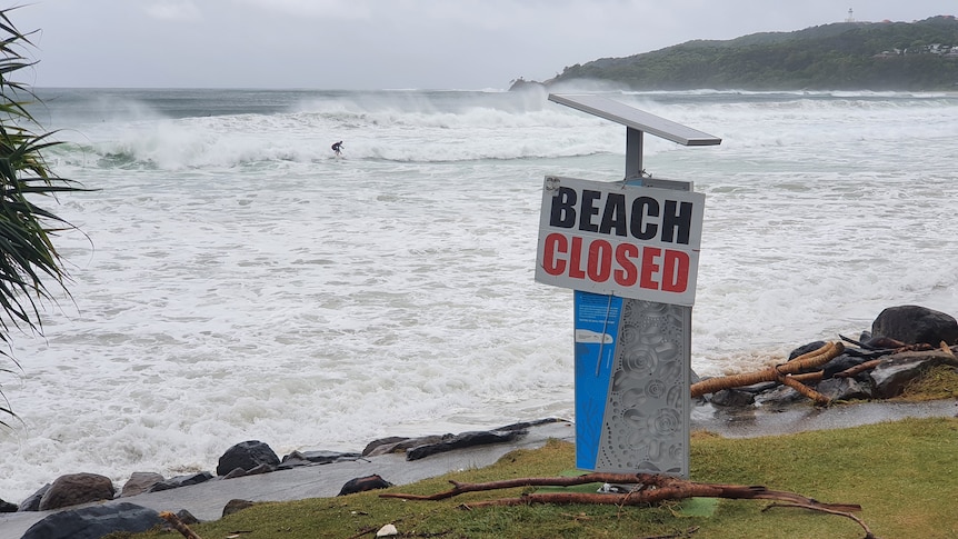 A beach covered in water with a 'closed sign' in the foreground.