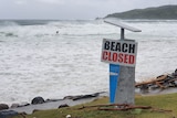 A beach covered in water with a 'closed sign' in the foreground.