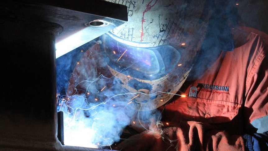 A person wearing a full-faced helmet welds.