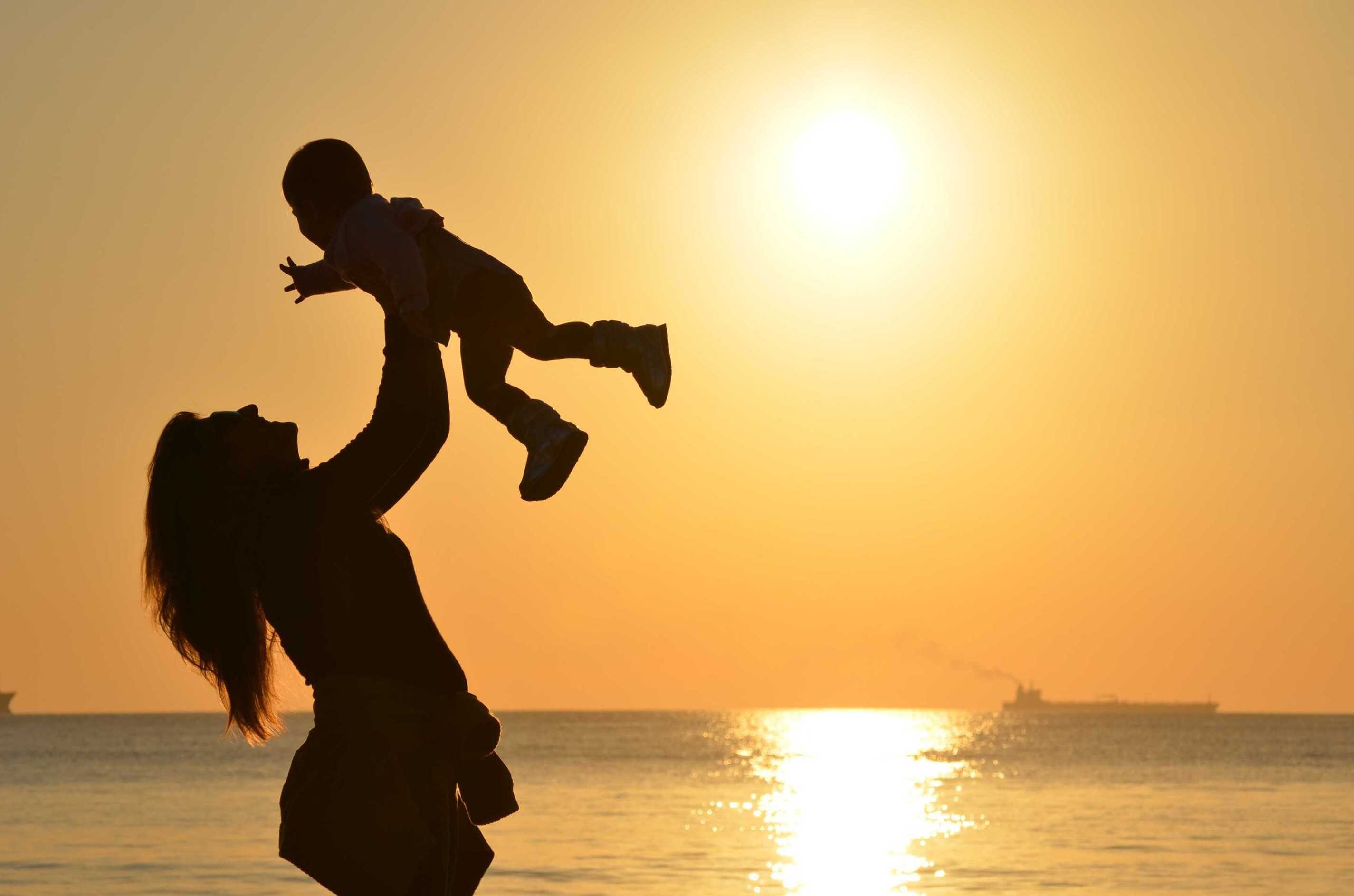 Silhouette of woman holding child in the air for a story about how people dealt with motherhood indecision.