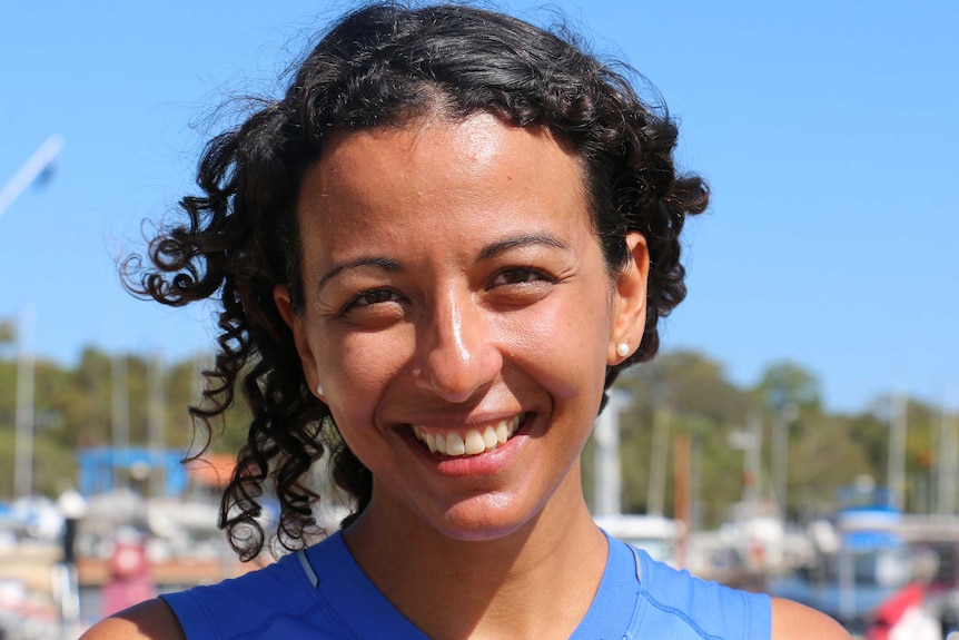 A headshot of a woman in a blue top smiling with boats in the background.