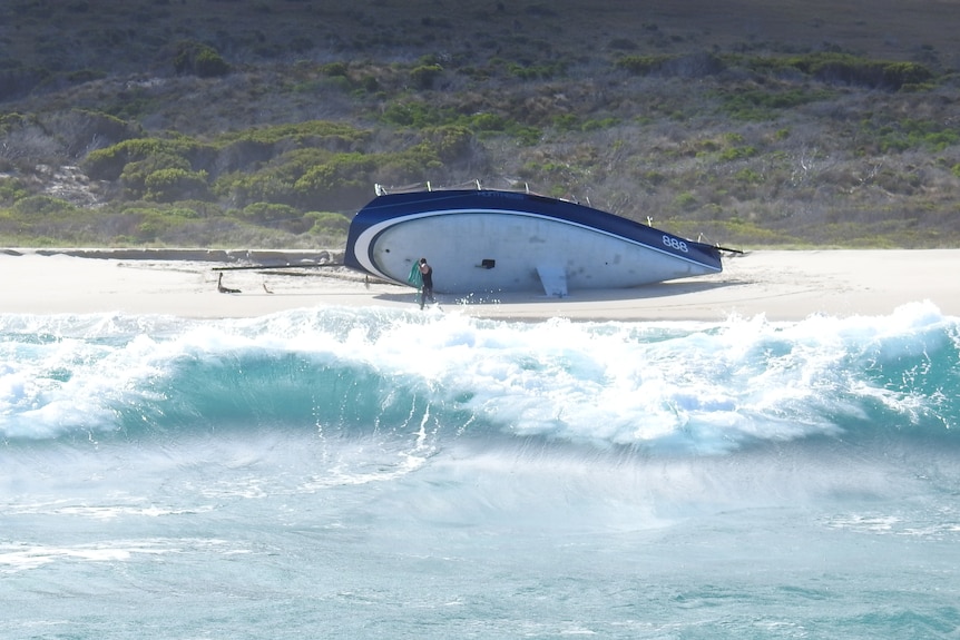 Yacht on its side on a beach with waves in foreground.