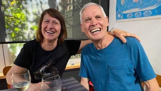 A man in a blue shirt and a woman in a black shirt sit at a table smiling
