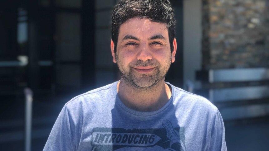 Man with dark hair and beard and wearing a blue t-shirt.