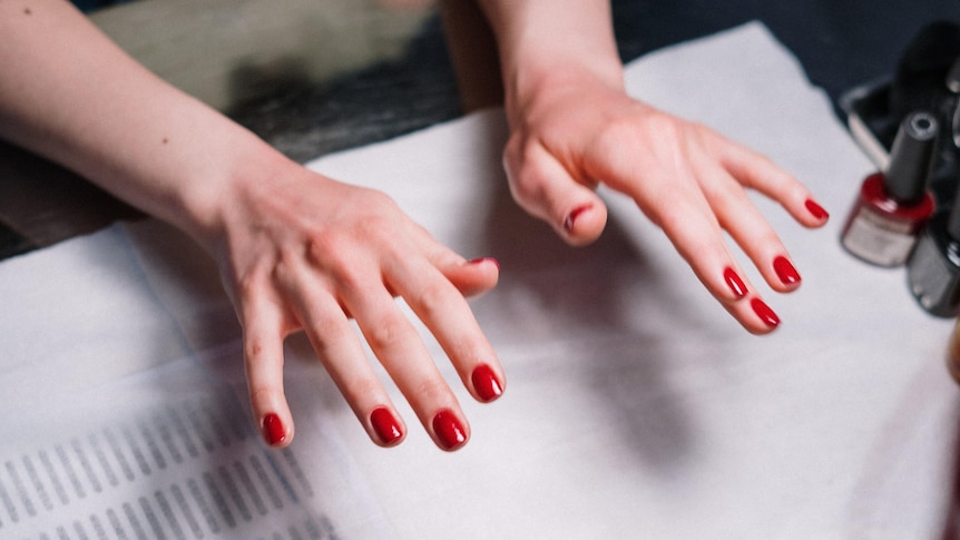A woman holds up her freshly painted red fingernails at a nail salon