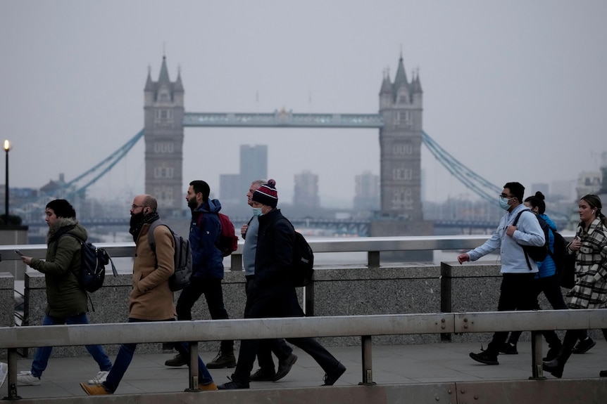 People wearing face masks walk over London Bridge with the Tower Bridge in the background.