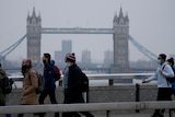 People wearing face masks walk over London Bridge with the Tower Bridge in the background.