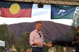 Nigel Scullion stands in front of Uluru under Aboriginal and Torres Strait Islander flags.