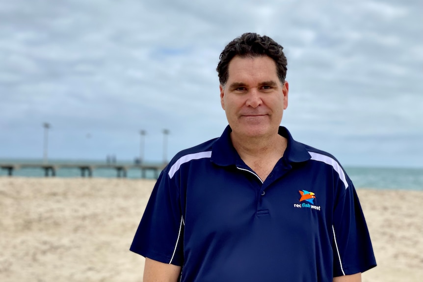 A man stands on the beach with a jetty behind him