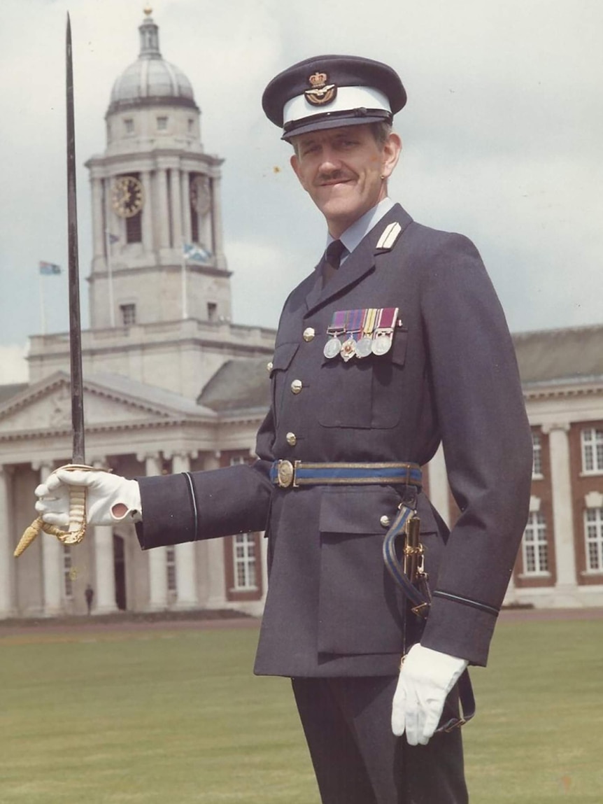 Alan holding a military sword while in Royal Air Force uniform in front of an old building.