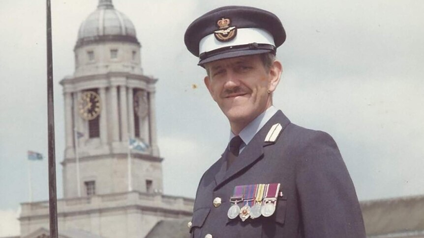 Alan holding a military sword while in Royal Air Force uniform in front of an old building.