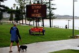 A man walking a dog near the beach walks part an electronic sign that reads: "Stay at home"