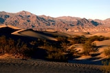 Sand dunes in the foreground, rocky mountains in the background.